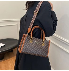 Brown monogram tote bag with gold hardware and wide jacquard strap worn by a model
