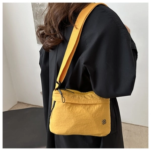 Detail showing bright yellow nylon shoulder bag with black strap and floral metallic emblem