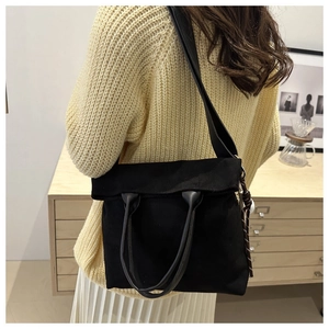 Close-up of black canvas tote bag with folding top worn by a model in a yellow sweater