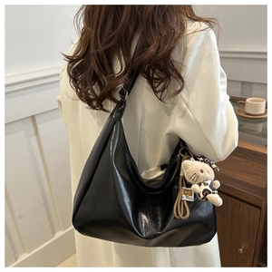Macro detail of black PU leather hobo bag with a cute plush cat charm on the strap