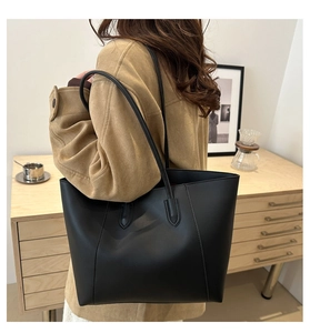 Detail of minimalist black leather tote bag worn by a model in a warm indoor setting
