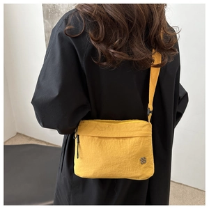 Detail of a bright yellow crossbody bag with a clover logo on a black outfit background