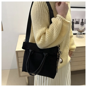Detailed shot of black canvas tote bag with leather handles and baseball charm accessory
