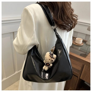 Detail of glossy black hobo bag on shoulder featuring a leopard-print kitty charm