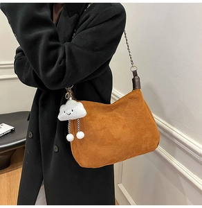 Detail of tan suede hobo bag with metal chain strap and a white cloud plush charm