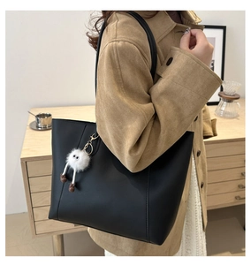 Close-up of minimalist black tote bag featuring a cute white plush ball bag charm detail