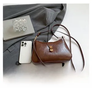Détail d'un sac demi-lune vintage marron avec fermoir doré sur une veste grise