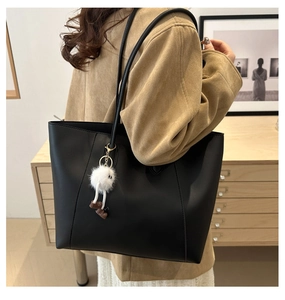 Detail of a black matte leather tote bag featuring a cute white plush doll charm