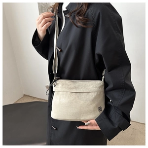 Detail of a cream nylon crossbody bag with floral logo on a black trench coat model