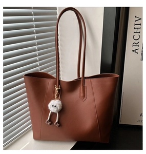 Close-up of brown faux leather tote bag featuring a cute white plush monster charm