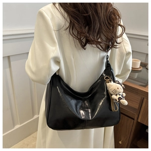 Detail of high-gloss black crescent tote bag with silver zipper and plush kitten charm