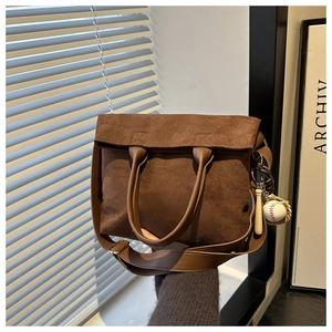 Detail of dark brown suede tote bag with leather straps and baseball charm accessory