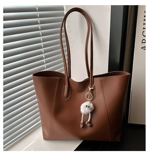 Detail of caramel brown tote bag with smooth texture and long-legged plush doll charm
