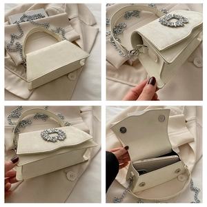 Detail view of cream handbag showing rhinestone buckle, metal chain, and magnetic closure