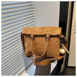 Detail view of brown faux suede tote bag with stylish baseball charm and wide shoulder strap