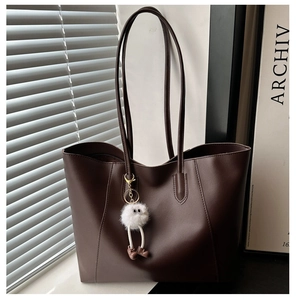 Detail of minimalist dark brown leather tote bag with fluffy white plush charm