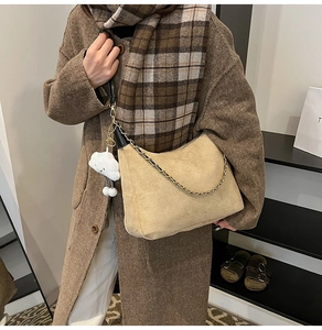 Close-up of beige suede hobo bag with gold chain strap and fluffy cloud pendant