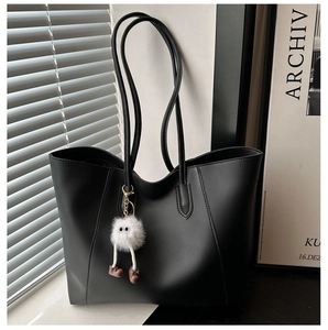 Detail of black leather tote bag featuring a cute white plush monster charm decoration