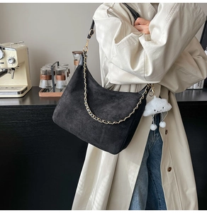 Detail of black suede crescent bag featuring gold chain and white cloud plush charm