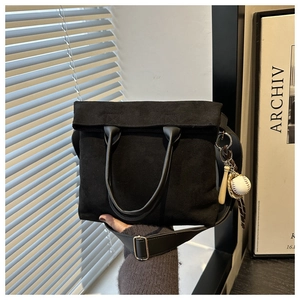 Close-up of black suede tote bag with leather handles and baseball charm detail