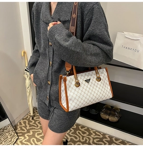 Detail view of stylish patterned tote bag with metal brand tag and woven strap on model