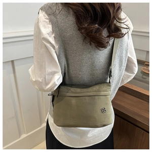 Detail of olive green nylon crossbody bag showing the silver flower logo and texture