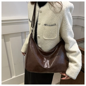 Detail of a large brown glossy leather tote bag with wide shoulder strap for women