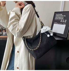 Detail of black matte hobo bag with gold chain and white cloud plush charm on trench coat