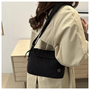 Detail of minimalist black nylon crossbody bag with silver flower logo and smooth zipper