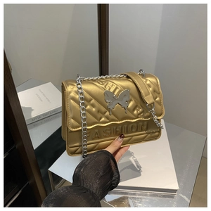 Détail du sac matelassé doré avec fermoir papillon et bandoulière en chaîne argentée