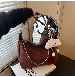 Detail of dark brown suede shoulder bag with gold chain and white plush cloud charm
