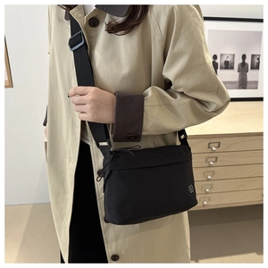 Close-up of black nylon crossbody bag with silver floral logo on khaki trench coat