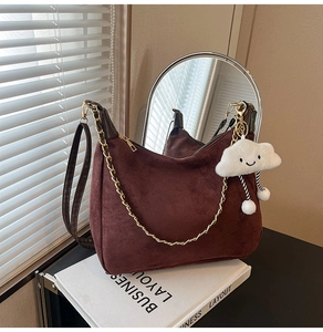 Detail of dark brown suede handbag with golden chain strap and a cute cloud charm