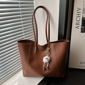 Brown minimalist leather tote bag for women with chic white plush charm on window sill