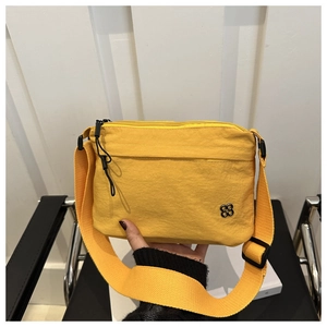 Detailed shot of yellow nylon crossbody bag featuring petal-shaped metal logo and wide strap