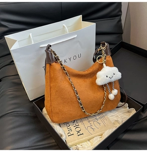 Detail of orange-brown hobo bag with suede texture, chain strap, and cloud charm
