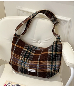 Detail shot of a brown plaid tweed crescent bag with wide strap and white fabric label