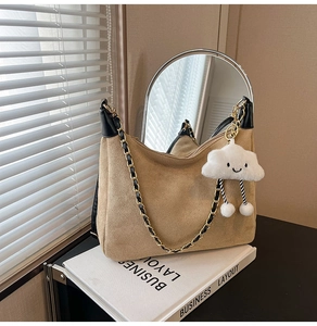 Detail of khaki suede shoulder bag with chain strap and cute cloud charm on white books