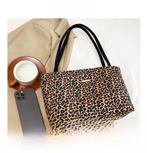 Detail view of leopard print tote bag with golden logo plaque and black straps