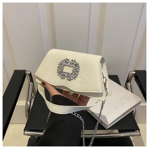 Close-up of beige square handbag featuring a large sparkling rhinestone buckle and chain