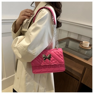 Sac bandoulière rose fuchsia avec boucle papillon et chaîne porté par un mannequin