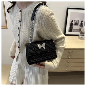 Vue détaillée du sac bandoulière noir brillant avec breloque papillon et bandoulière chaîne