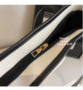 Close-up of smooth gold metal zipper and black trim on white textured leather tote bag