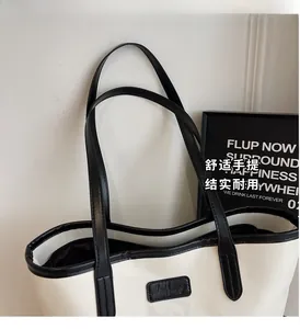 Detail of minimalist tote bag showing black handle stitching and contrast logo marking