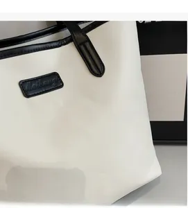 Detail of white tote bag featuring black piping and a stitched shield logo emblem