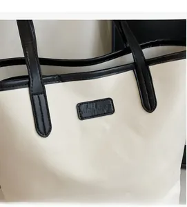 Detailed close-up of cream tote bag with black trim and embossed leather logo tag