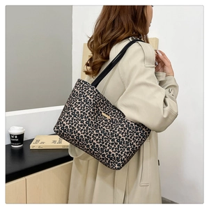 Detail of leopard print tote bag featuring a golden logo plate and sturdy shoulder straps