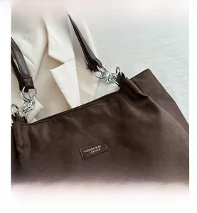 Close-up of brown suede tote bag with silver chain strap on a beige blazer