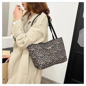 Detail of leopard print tote bag with gold logo plaque on a beige trench coat