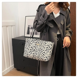 Detail of a leopard print canvas tote bag with black straps and a golden metal emblem